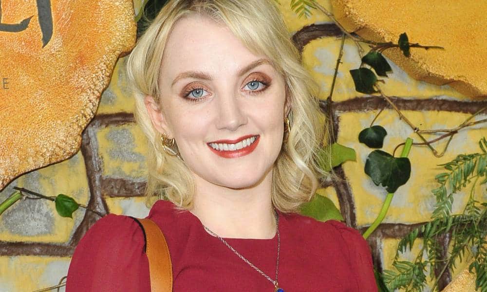 Evanna Lynch smiles at the camera while wearing a red outfit and a brown bag strap can be seen on her shoulder
