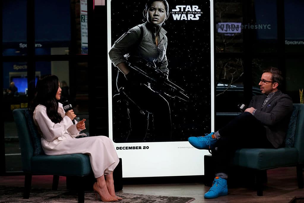 POC actress, Kelly Marie Tran, sits on the left-hand side of the stage, interviewed by a male presenter, a picture of her Star Wars character in between them. 