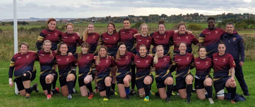 Players with the East London Vixens wear red rugby uniforms as they kneel or stand for a photograph together