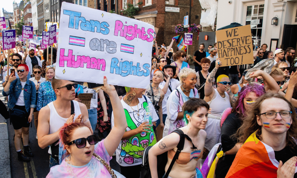 Several people hold up sign in support of the trans community and LGBTQ+ people during a parade march