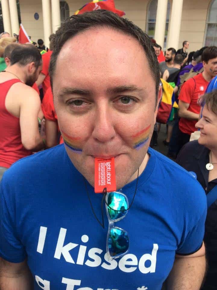 Colm Howard-Lloyd wearing a t-shirt that reads "I kissed a Tory" at a Pride event. He has rainbow colours painted on his face.